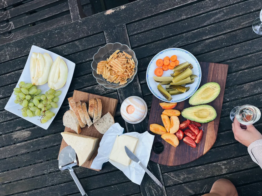 Stůl s hrozny, melounem, avokádem, sýrem, chlebem a chipsy, zapálená svíčka.