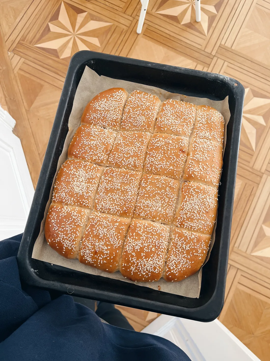 Černý plech se čtyřmi řadami zlatých sezamových houstiček na dřevěné podlaze.