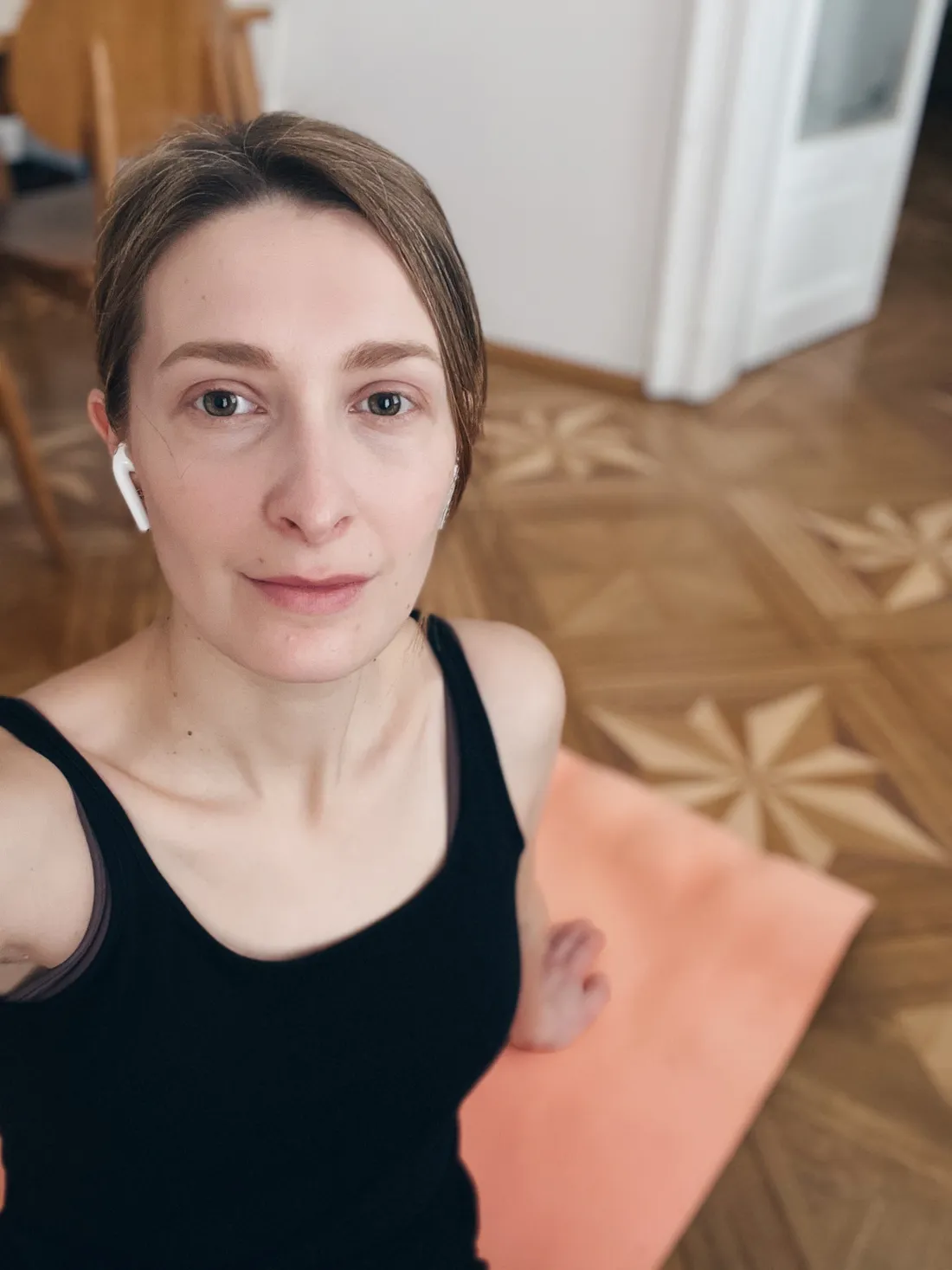 Selfie ženy se sluchátky na oranžové podložce na parketách s hvězdovým vzorem.