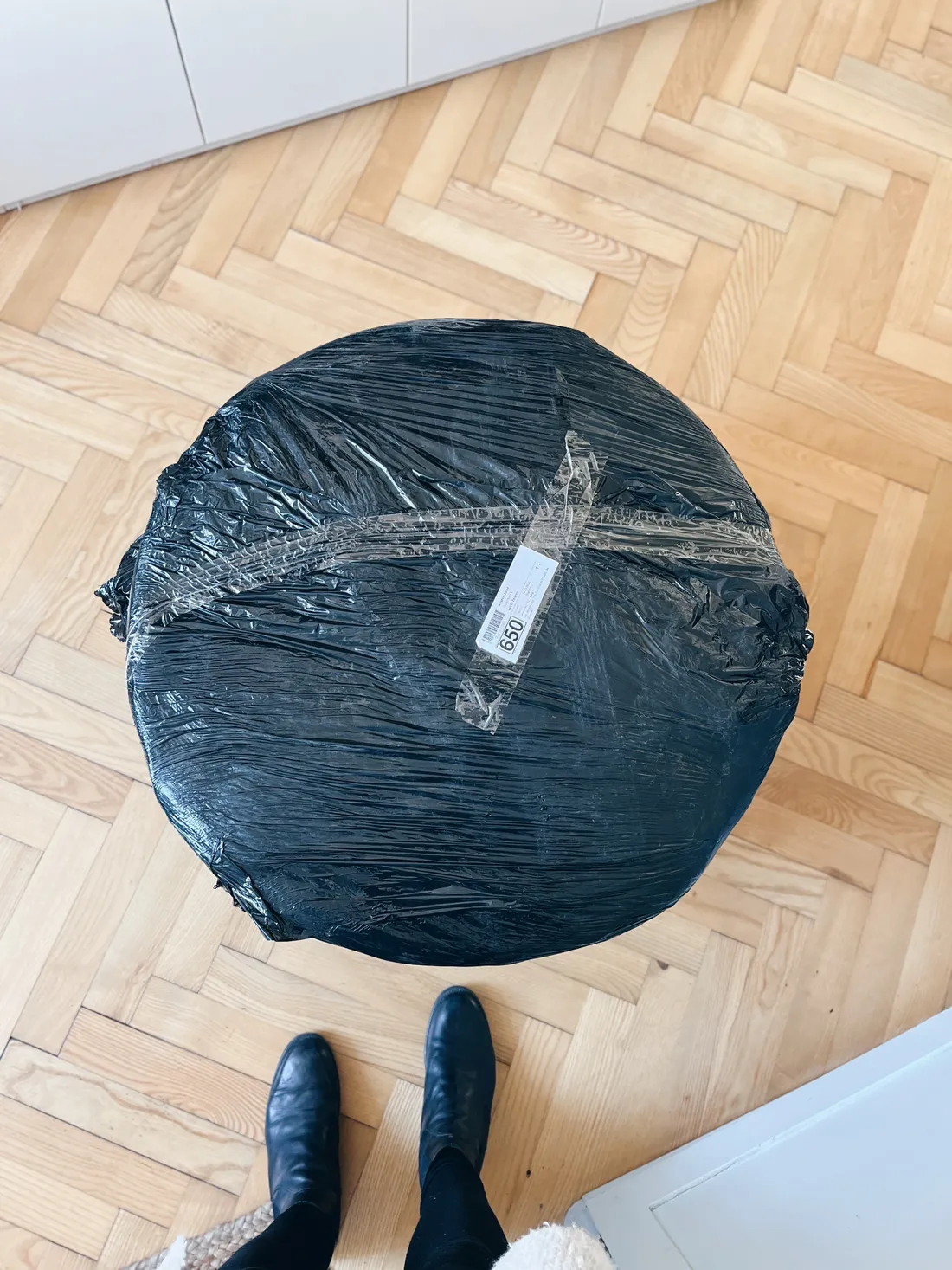 Kruhový balík zabalený v černé fólii se štítkem 650 na parketové podlaze.