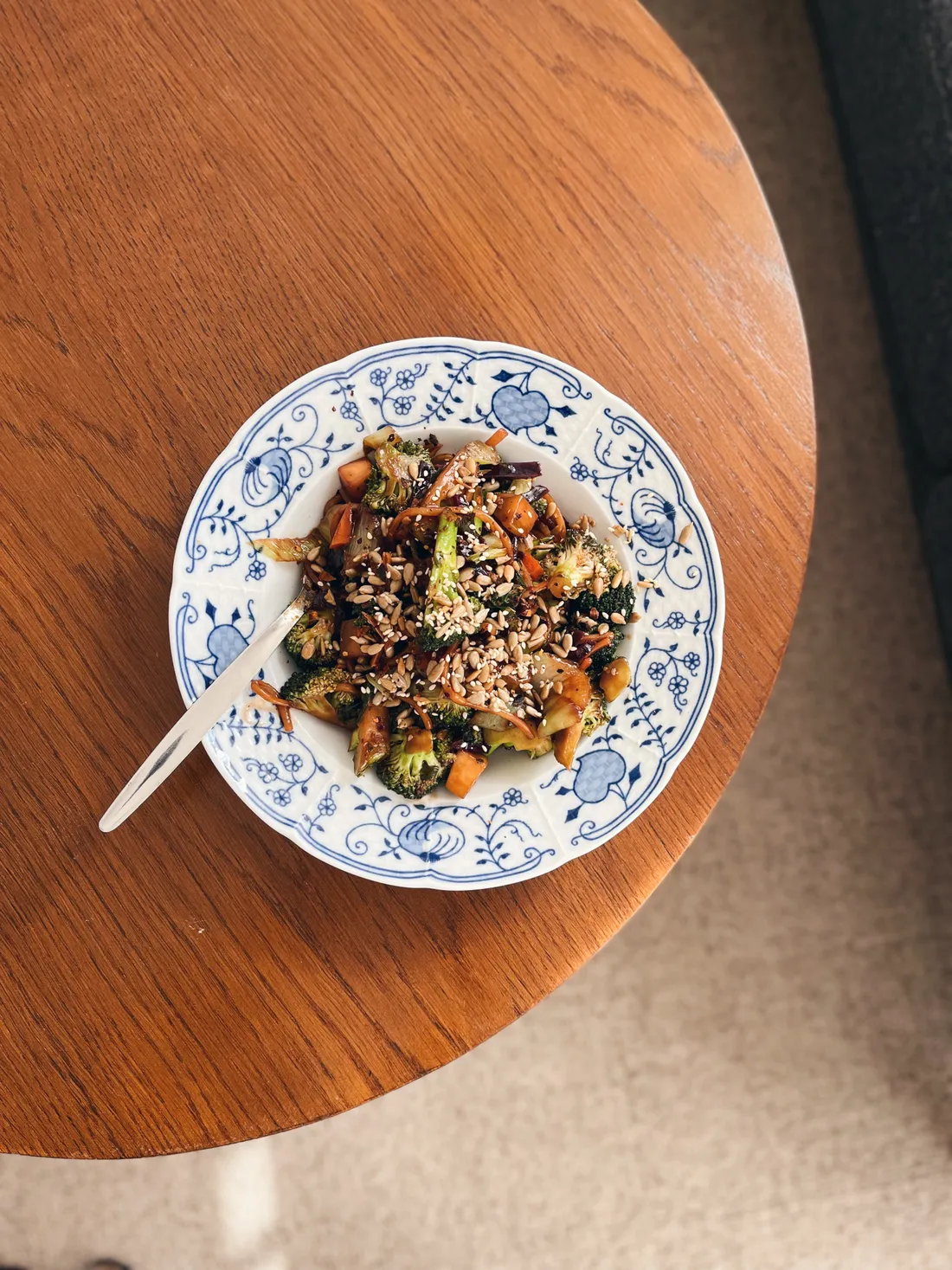 Brokolice s mrkví a slunečnicovými semínky na modrobílém talíři na dřevěném stole.