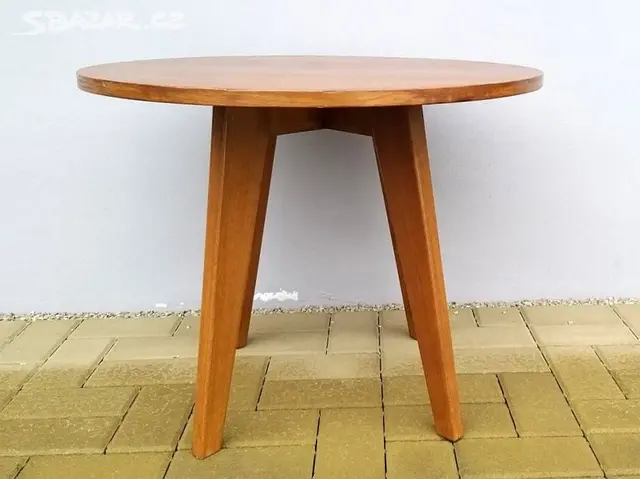 Kulatý retro dřevěný stůl se čtyřmi šikmými nohami na dlažbě u světlé zdi.