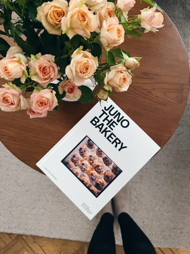 Kniha Juno the Bakery se šneci na obálce a kytice meruňkových růží na kulatém dřevěném stole shora.