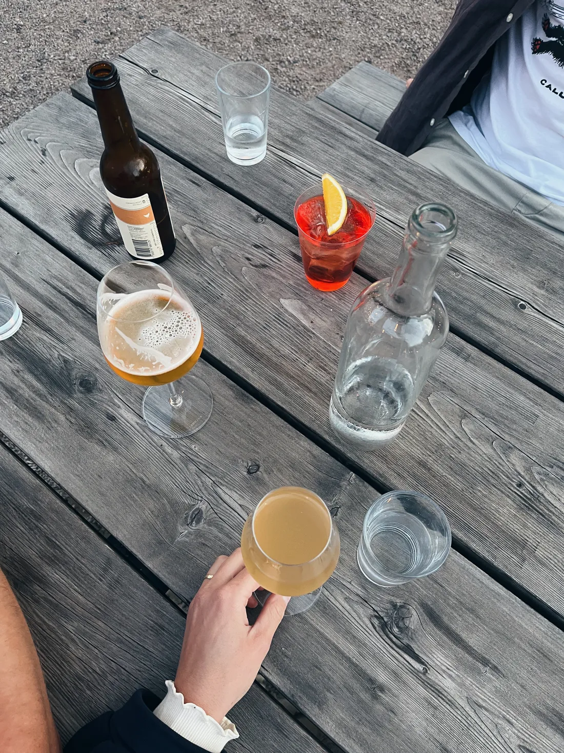 Piknikový stůl se sklenicemi piva, Aperol Spritz a vodou na dřevěném stole venku