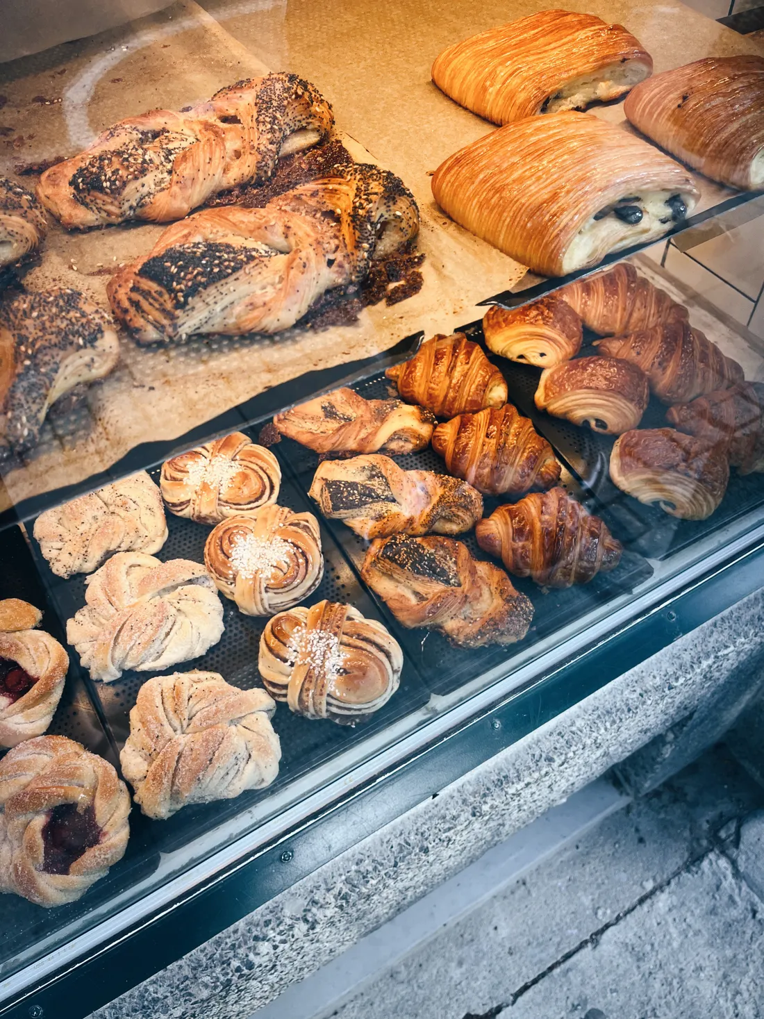 Výloha pekařství s croissanty, čokoládovými rolkami, šneky a makovým pečivem.