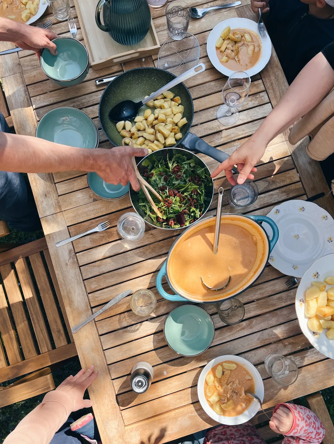 Venkovní oběd na dřevěném stole s oranžovou omáčkou, gnocchi, salátem a modrým nádobím.