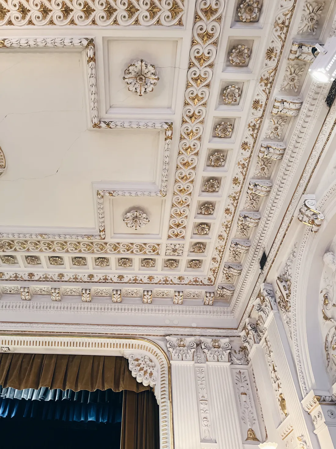 Zlacený štukový strop a balkon s červenými závěsy v historickém divadle.