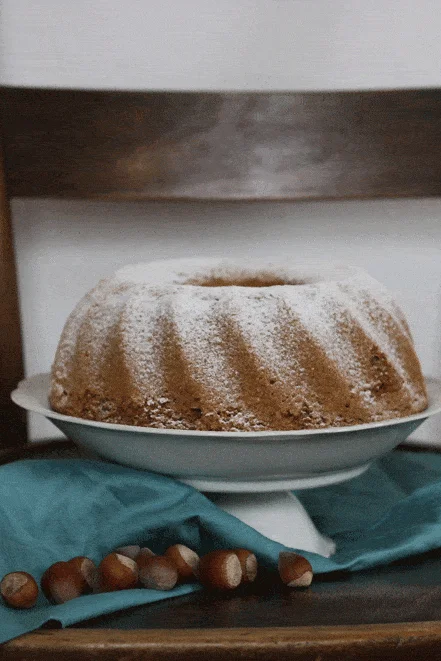 Ořechová bábovka sypaná moučkovým cukrem na podnosu na staré dřevěné židli s lískovými ořechy.
