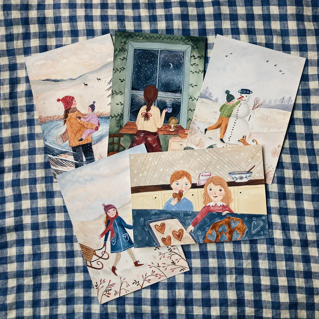 Pět zimních ilustrací na modrobílém kostkovaném ubrusu.
