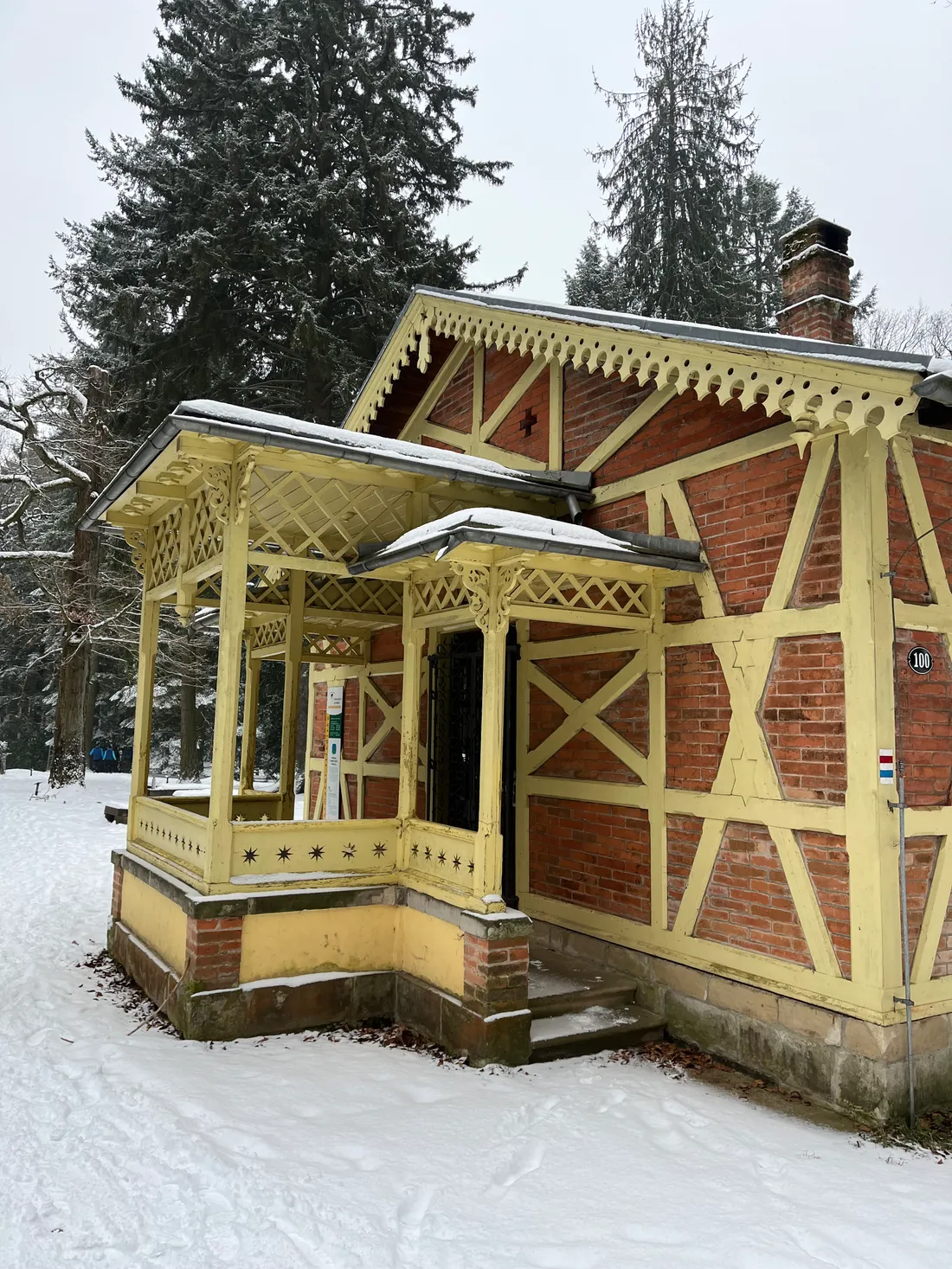 Zdobený cihlový domek se žlutým hrázděním a vyřezávanou verandou v zasněženém lese.