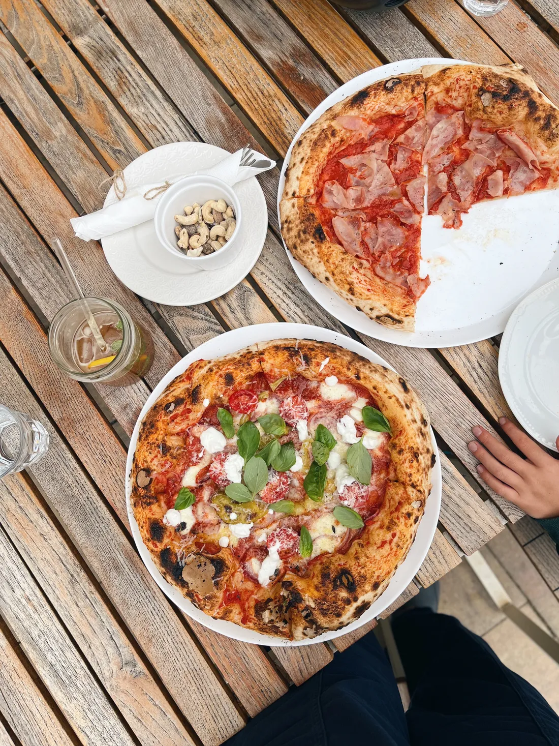 Dvě neapolské pizzy s mozzarellou a bazalkou na dřevěném stole, jedna částečně snědená.