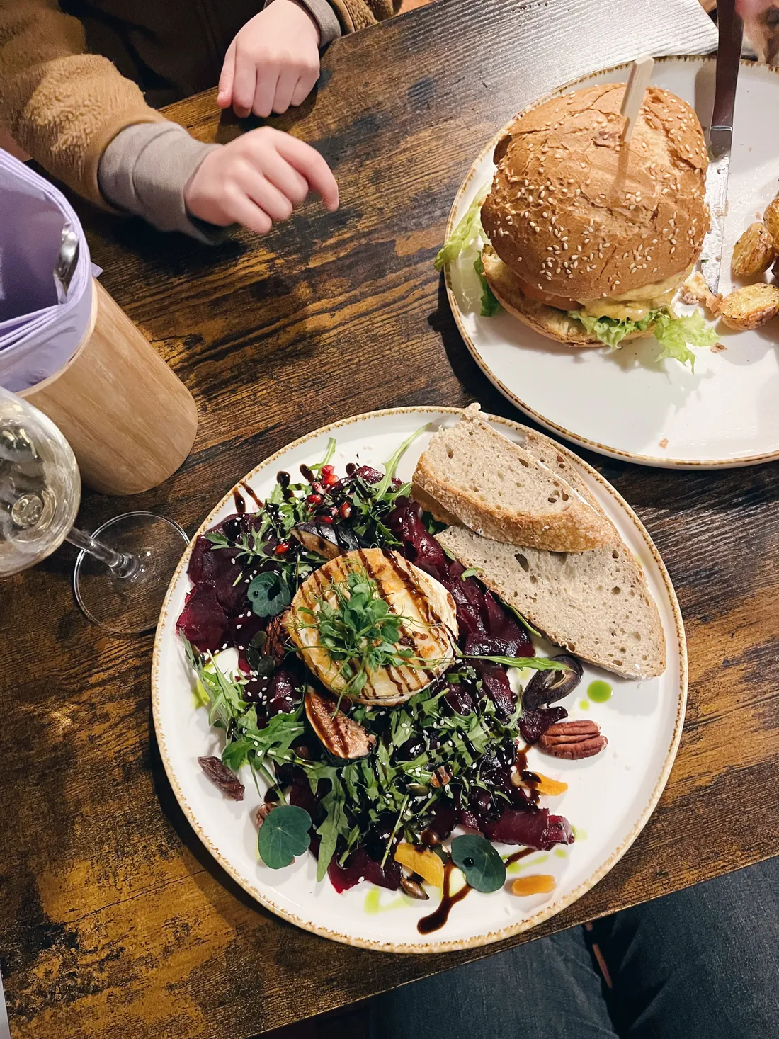 Salát s grilovaným sýrem, řepou a rukolou a burger se sýrem na dřevěném stole v restauraci.