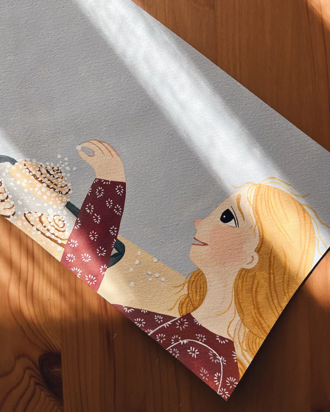Ilustrace dívky posypávající cukr na skořicové šneky na šedém papíru v paprscích slunce