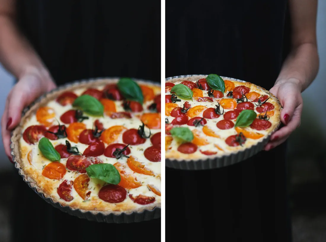 Upečený quiche s červenými a oranžovými cherry rajčátky a bazalkou v koláčové formě, servírovaný v rukou.