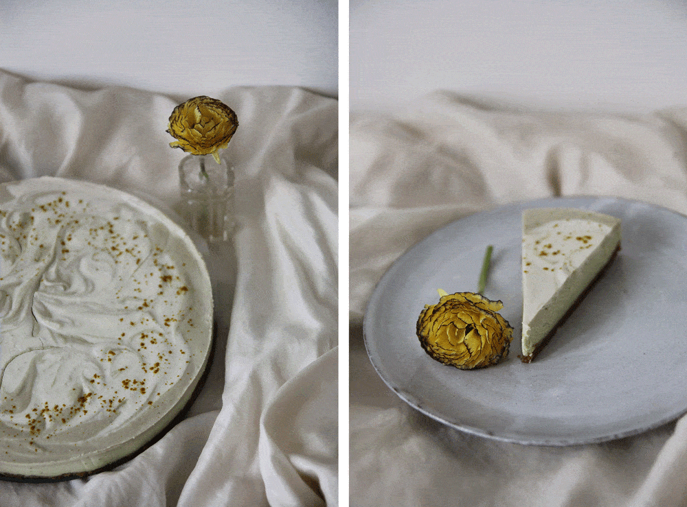 Celý kulatý raw avokádový cheesecake se žlutým práškem a řez na šedém talíři se žlutým květem na látce.