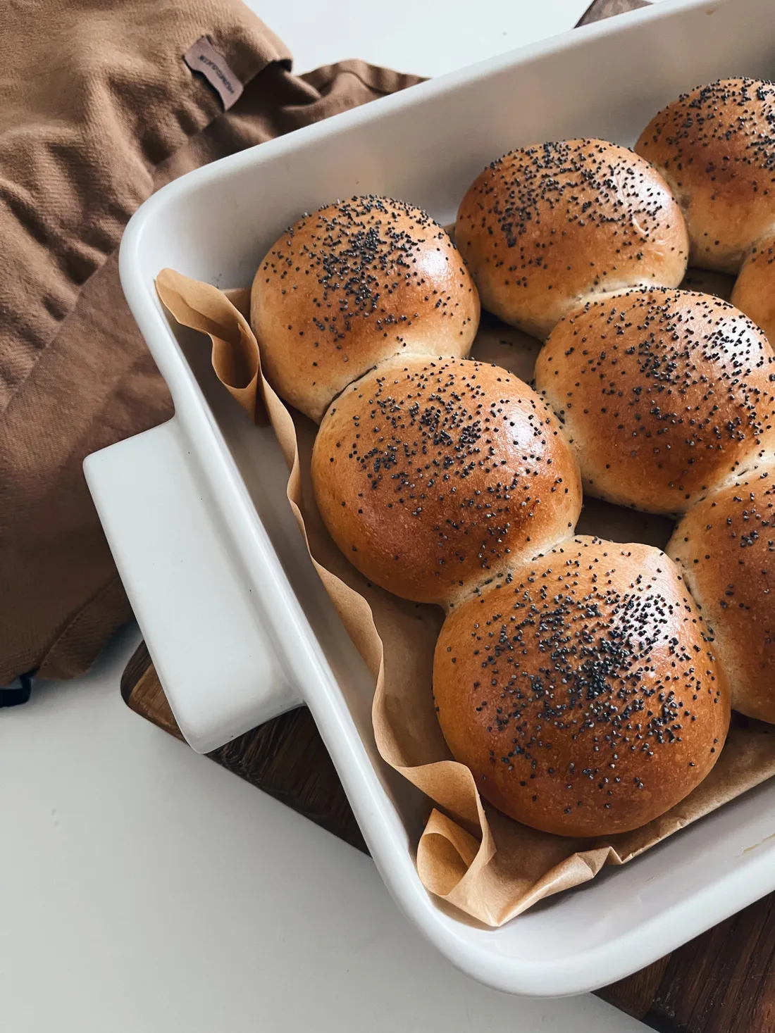 Zlatavé buchty posypané mákem v bílém keramickém pekáči na lněném ubrousku.