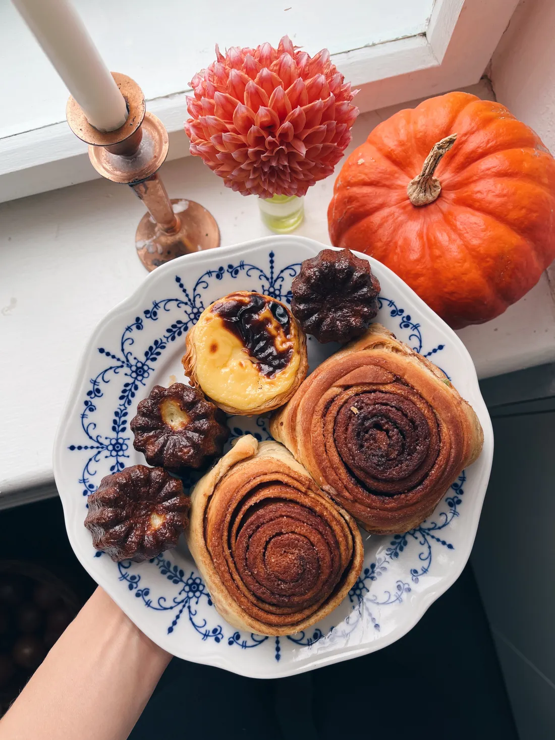 Talíř se skořicovými šneky, pastel de natou a canelés na parapetu s dýní