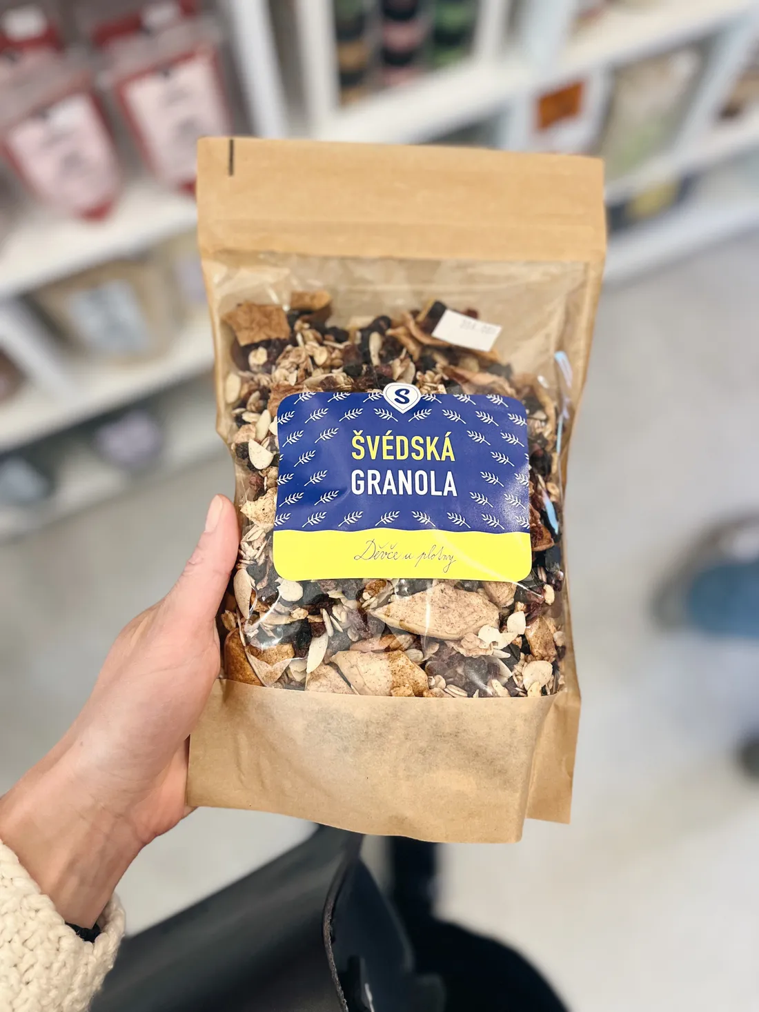 Ruka drží sáček Švédská granola Děvče u plotny v obchodě Světa plodů