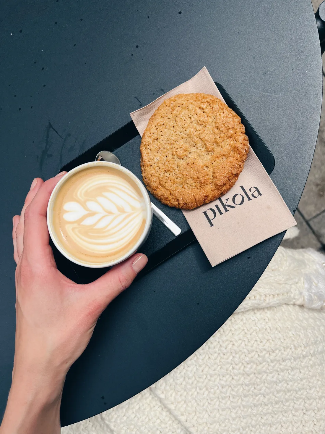 Kapučíno s latte art a velká sušenka Pikola na černém tácu