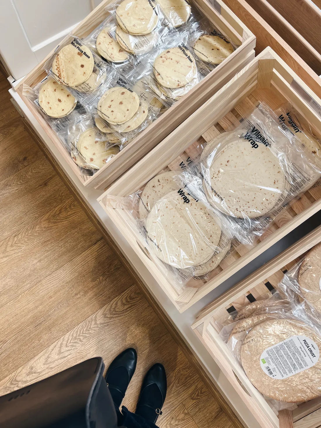 Bedny s produkty Vilgain v obchodě, pohled shora na nohy v černých botách
