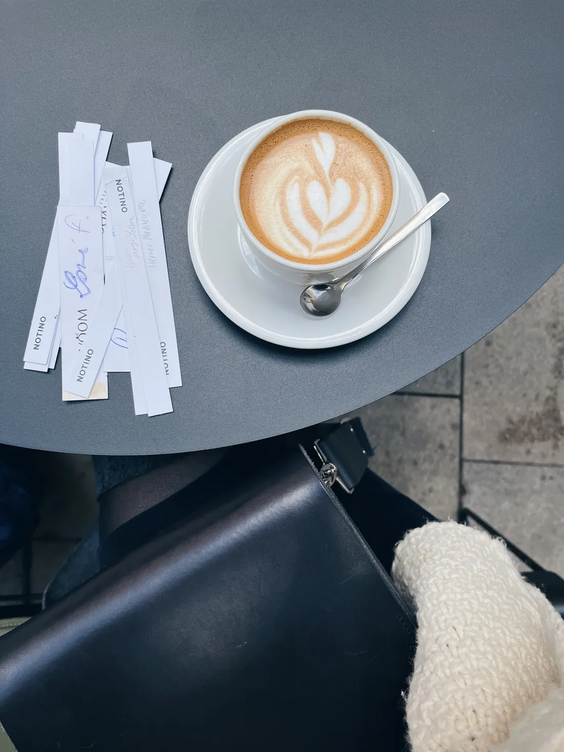 Šálek kávy s latte art a hromada parfémových testerů Notino na šedém stolku