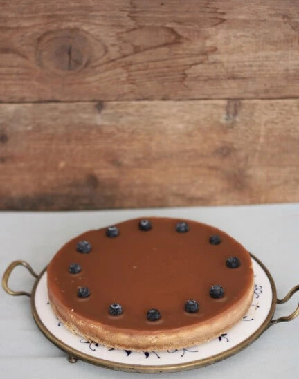 Skořicový cheesecake se slaným karamelem a borůvkami na bílém talíři v mosazném podnosu.