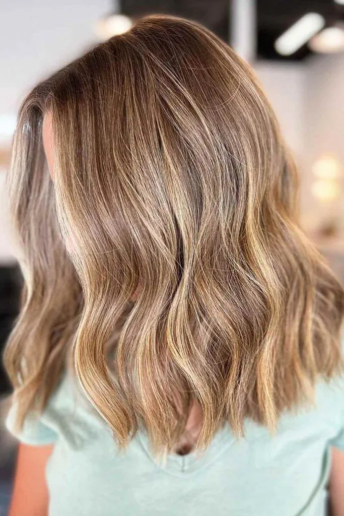 Světle hnědé vlasy s blond melírem ve volných vlnách, záběr z boku u okna.