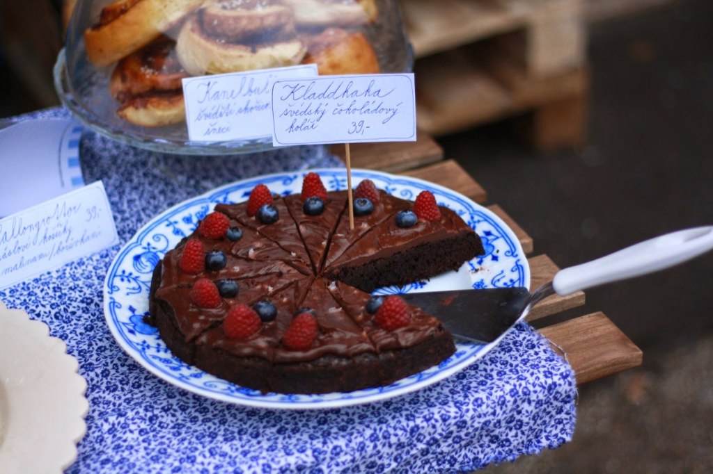 Kladdkaka na modrobílém talíři s malinami a borůvkami a cedulkou se švédským čokoládovým koláčem.
