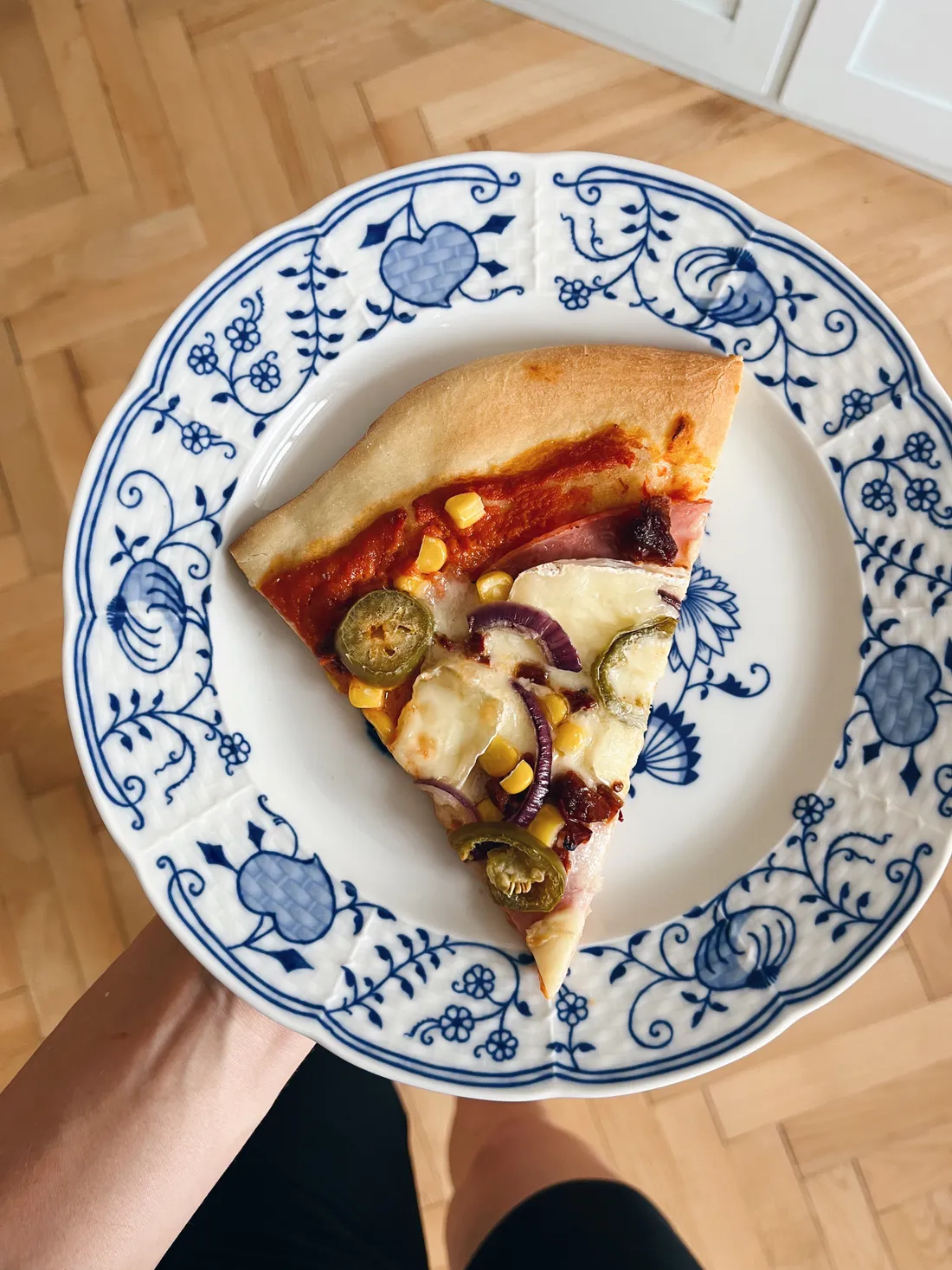 Trojúhelník pizzy s kukuřicí, cibulí, jalapeños a hermelínem na talíři s cibulovým vzorem.