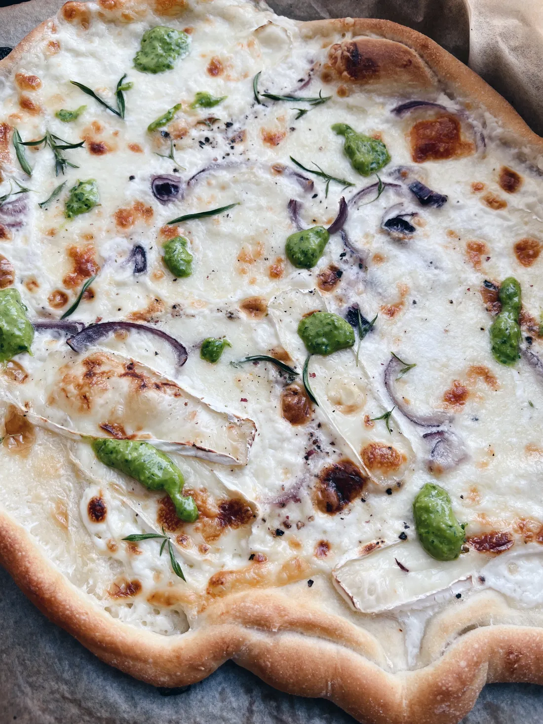 Bílá pizza s rozmarýnem, červenou cibulí, pestem a plísnivým sýrem na pečicím papíru.
