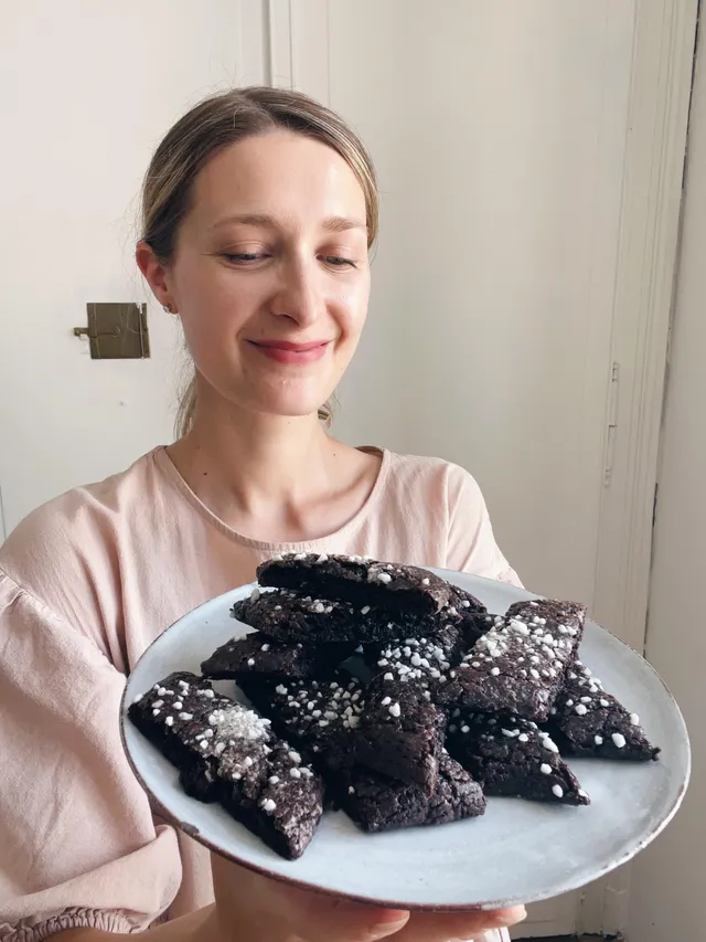 Žena drží bílý talíř se švédskými čokoládovými sušenkami chokladsnittar posypanými perlovým cukrem.