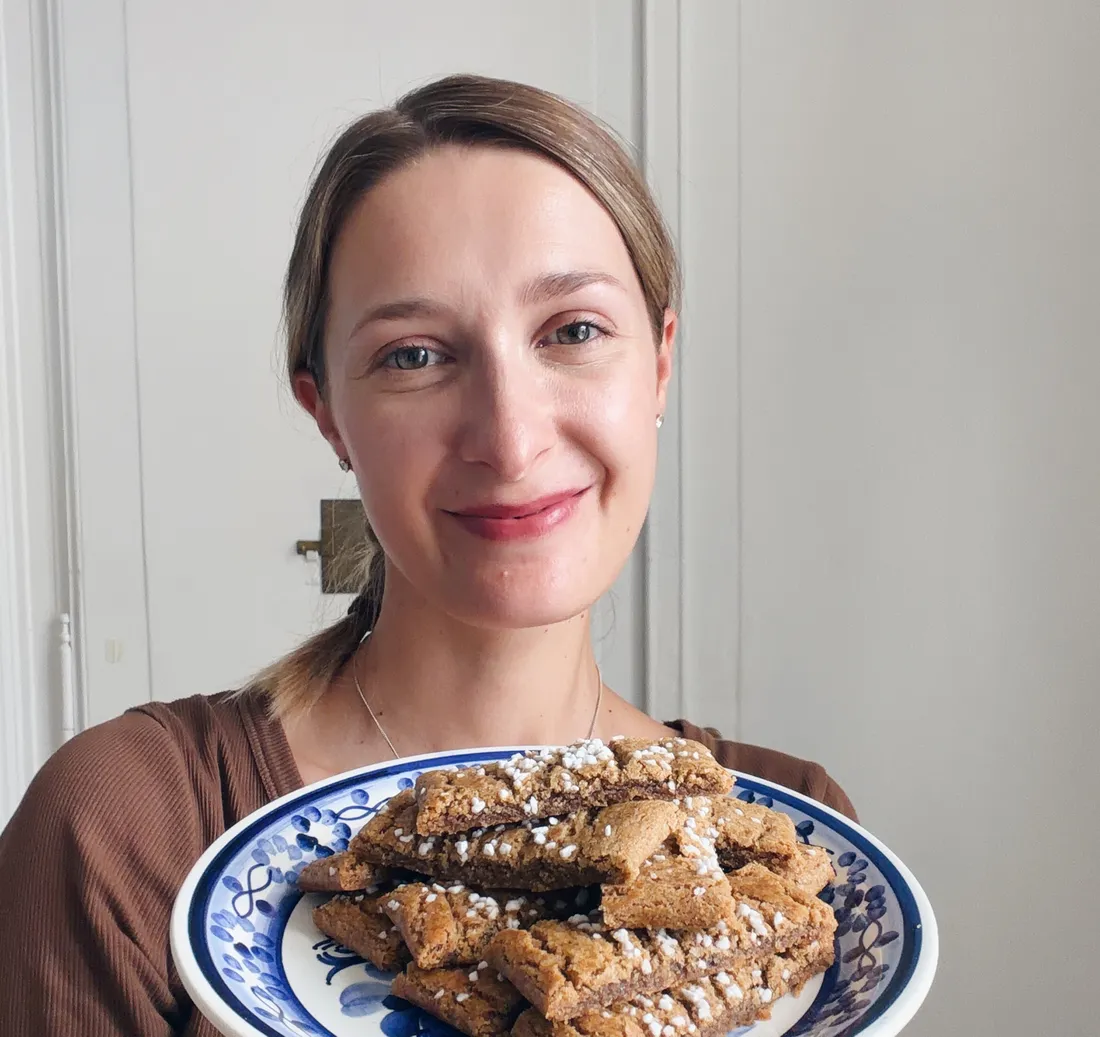 Žena s culíkem drží talíř se zlatými šikmými sušenkami posypanými perlovým cukrem na modrobílém porcelánu s květinovým vzorem.