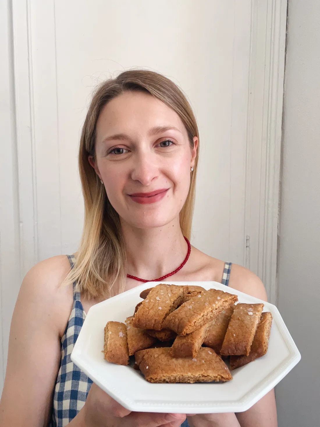 Žena drží bílý talíř se zlatavými proužkovými sušenkami upečenými z delších válečků.