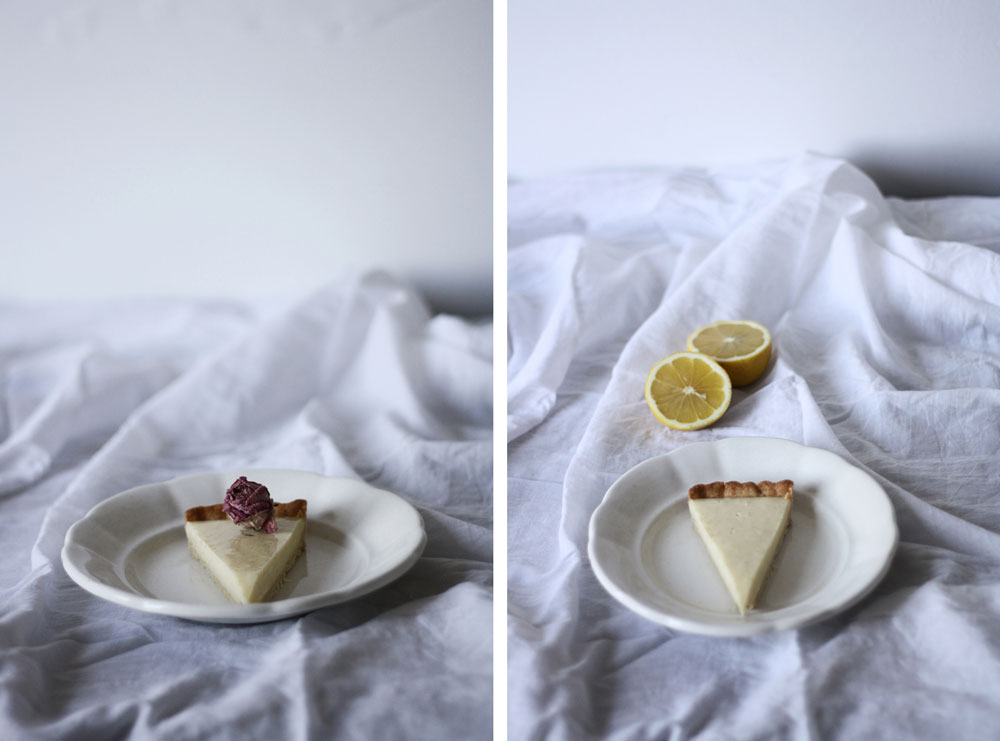 Řez citronového koláče na bílém talíři se sušeným květem a druhý záběr s polovinami citronu na zmačkaném ubrusu.
