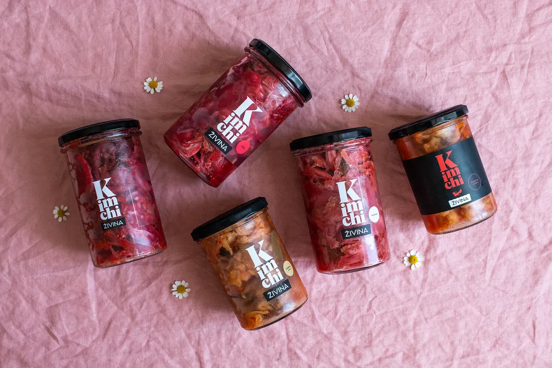 Sklenice tří druhů kimchi od Živiny na dřevěném stole v denním světle.