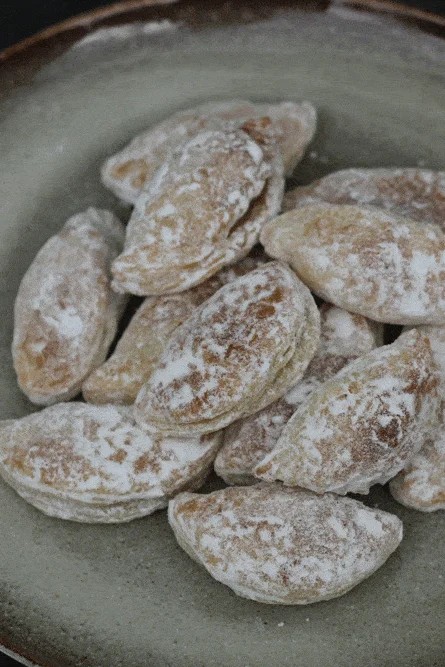 Tvarohové taštičky s hruškovými povidly posypané moučkovým cukrem na keramickém talíři.