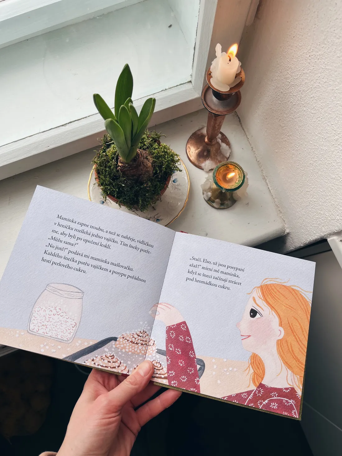 Otevřená dětská kniha Elsa s šneky, hyacint a svíčky na parapetu.