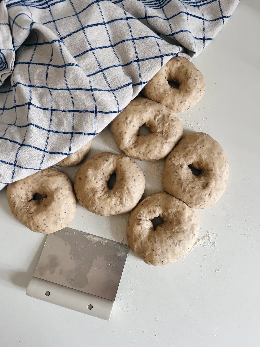 Šest syrových kroužků těsta na bílé lince pod modrobílým utěrkou, vedle stěrka.
