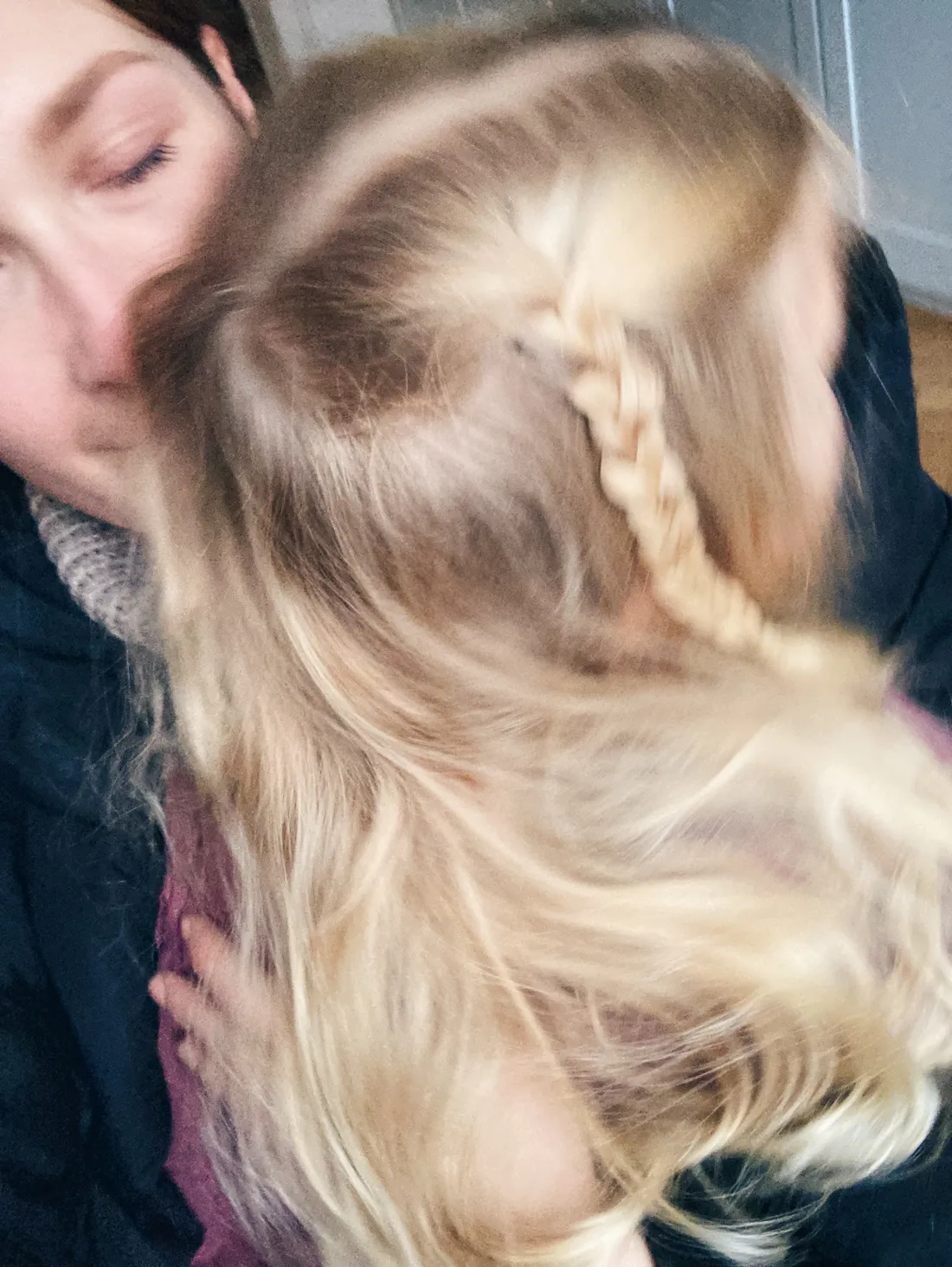 Žena objímá holčičku s dlouhými blond vlasy a copánkem, detail obličejů u sebe.