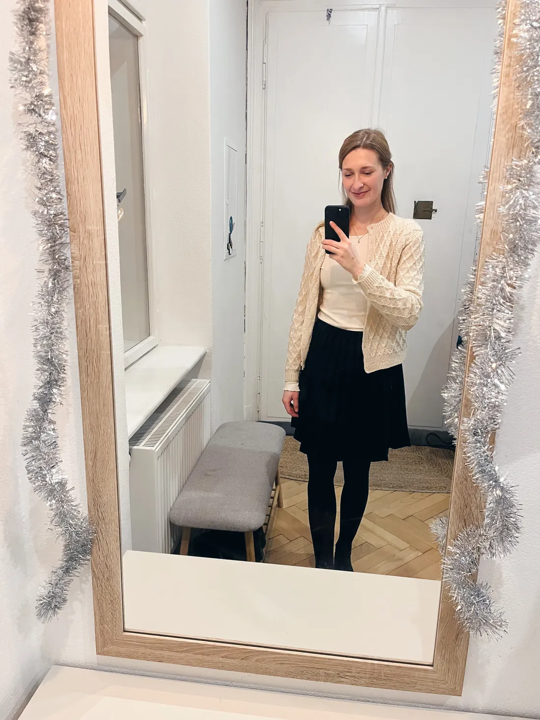 Žena v krémovém svetru a černé sukni v zrcadlové selfie, zrcadlo s cinkoty.