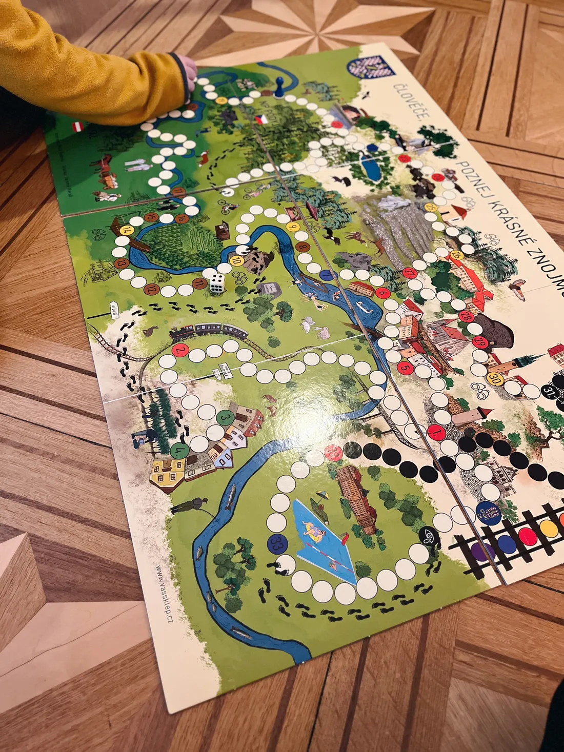 Desková hra Člověče, poznej krásné Znojmo na parketách s kostkou a modrou figurkou.