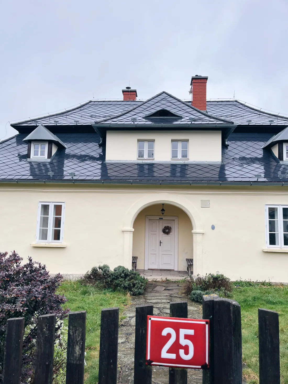 Rodinný dům s červenou střechou a štítovými okny, branka s číslem 25.