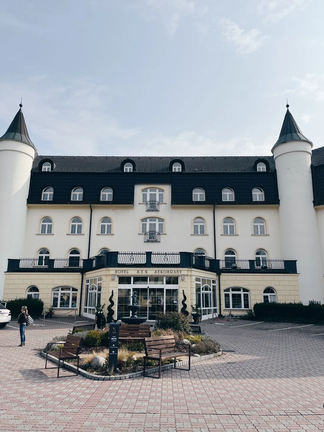 Hotel Sen v Senohrabech s bílou fasádou, věžičkami a nádvořím s lavičkami.