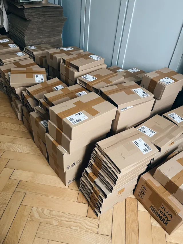 Hromada kartonových krabic s přepravními štítky na parketové podlaze s hvězdičkovým vzorem.