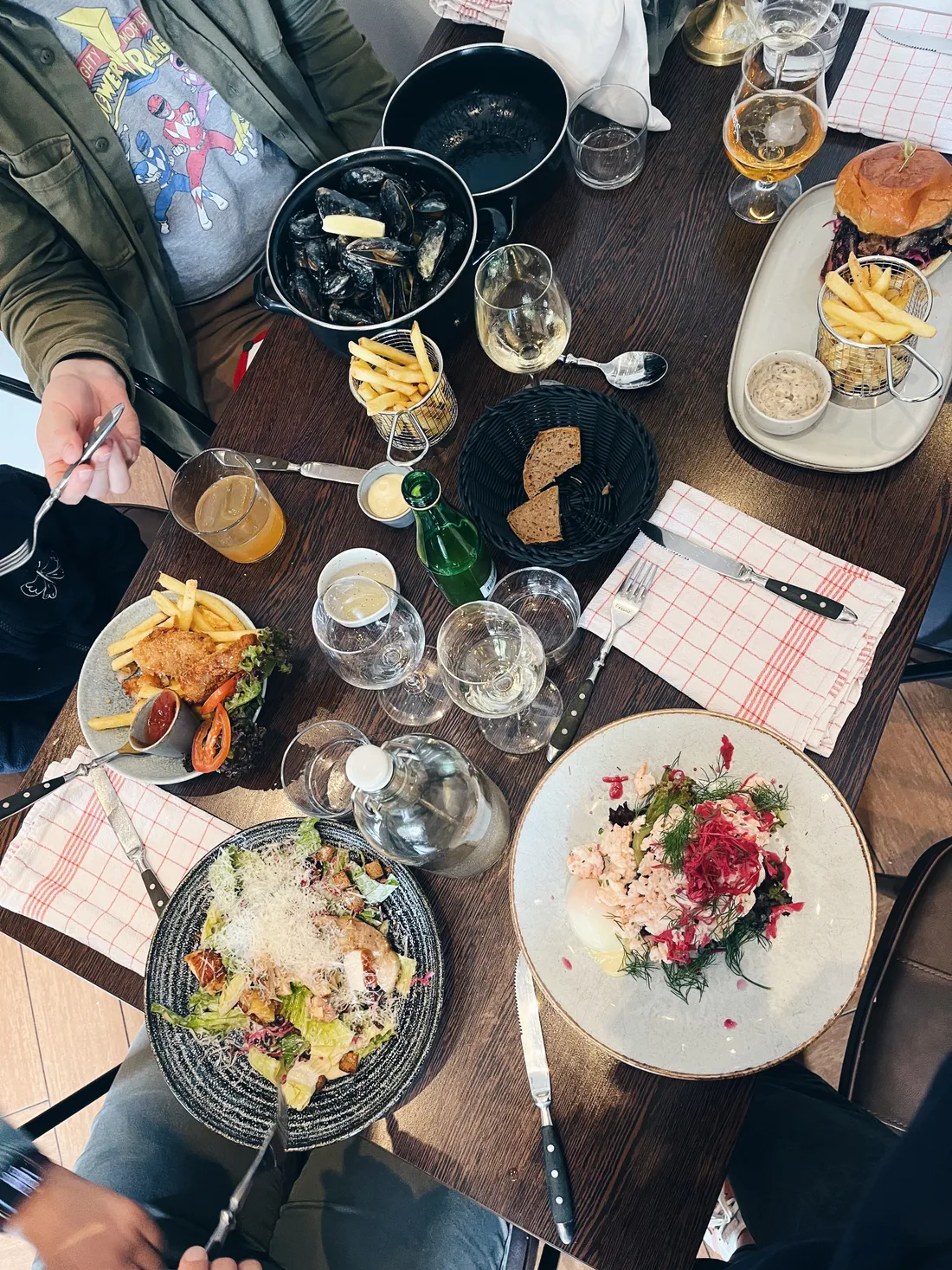 Stůl v restauraci s mušlemi, burgerem, saláty, vínem a pivem pro několik lidí.