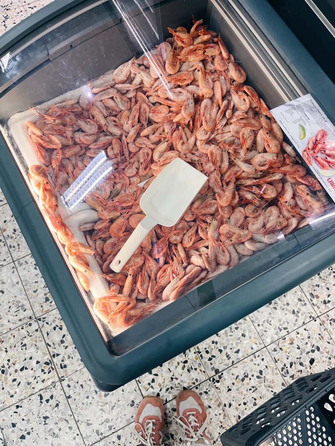 Mrazicí box v obchodě plný mražených růžových krevet, bílá naběračka na povrchu.