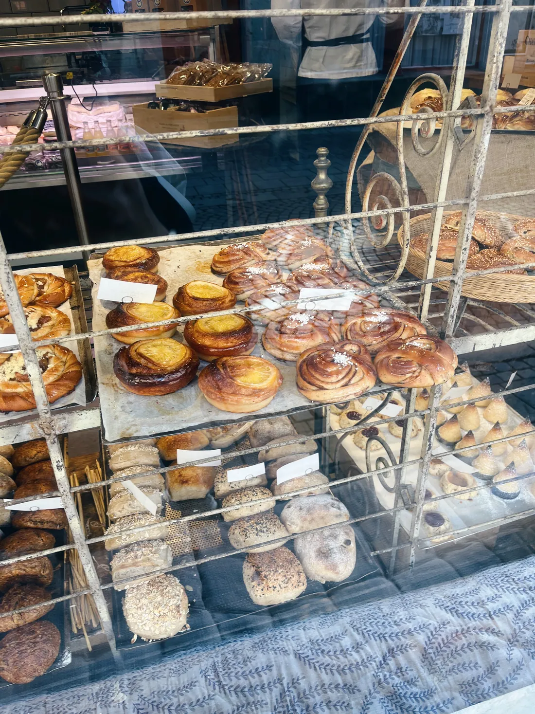 Výloha pekárny s koláči, skořicovými šneky a různými bulkami na bílém kovovém regálu.