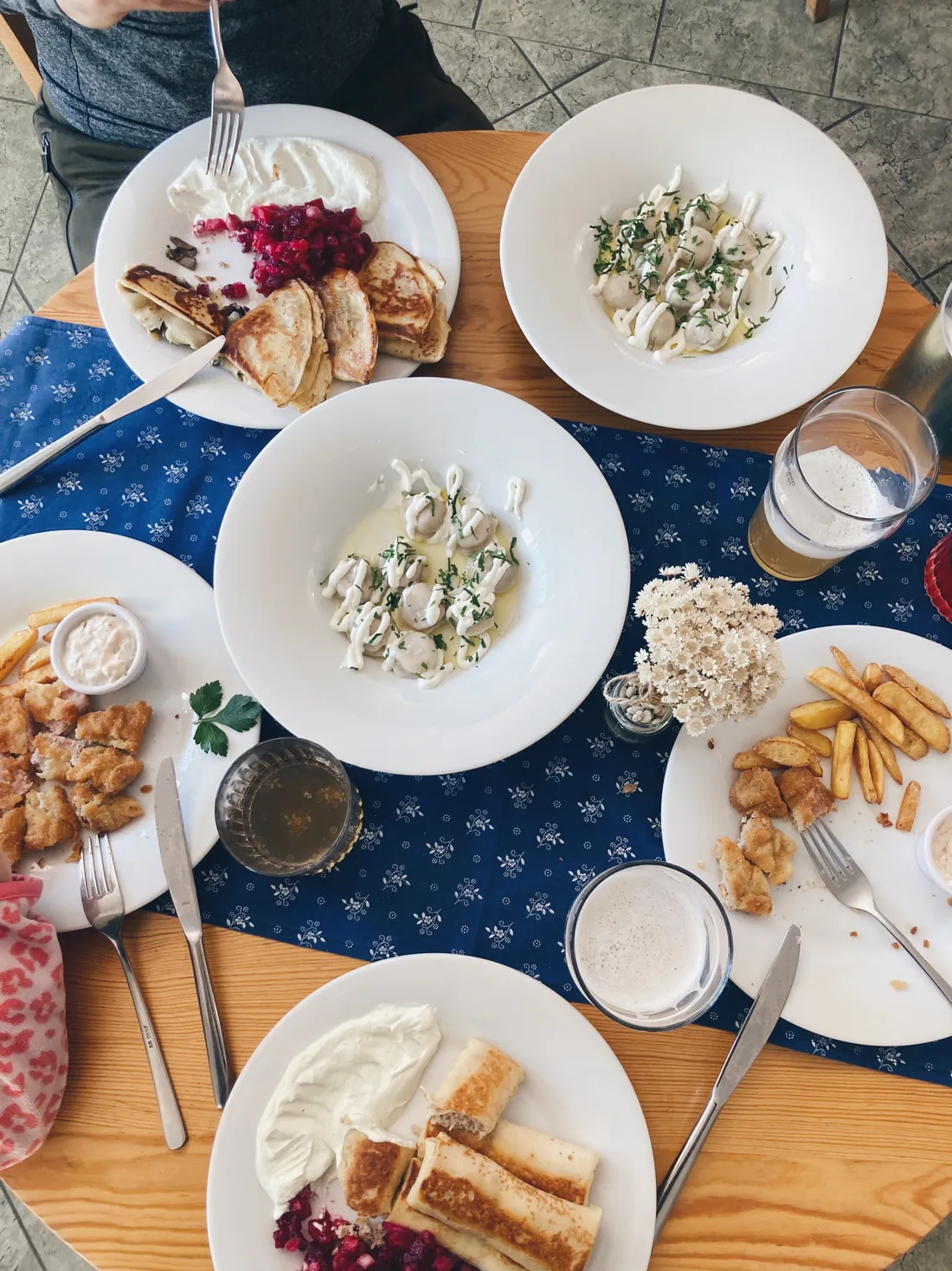Dřevěný stůl s pelmeněmi, bliny, smaženým jídlem, hranolky a pivem shora.