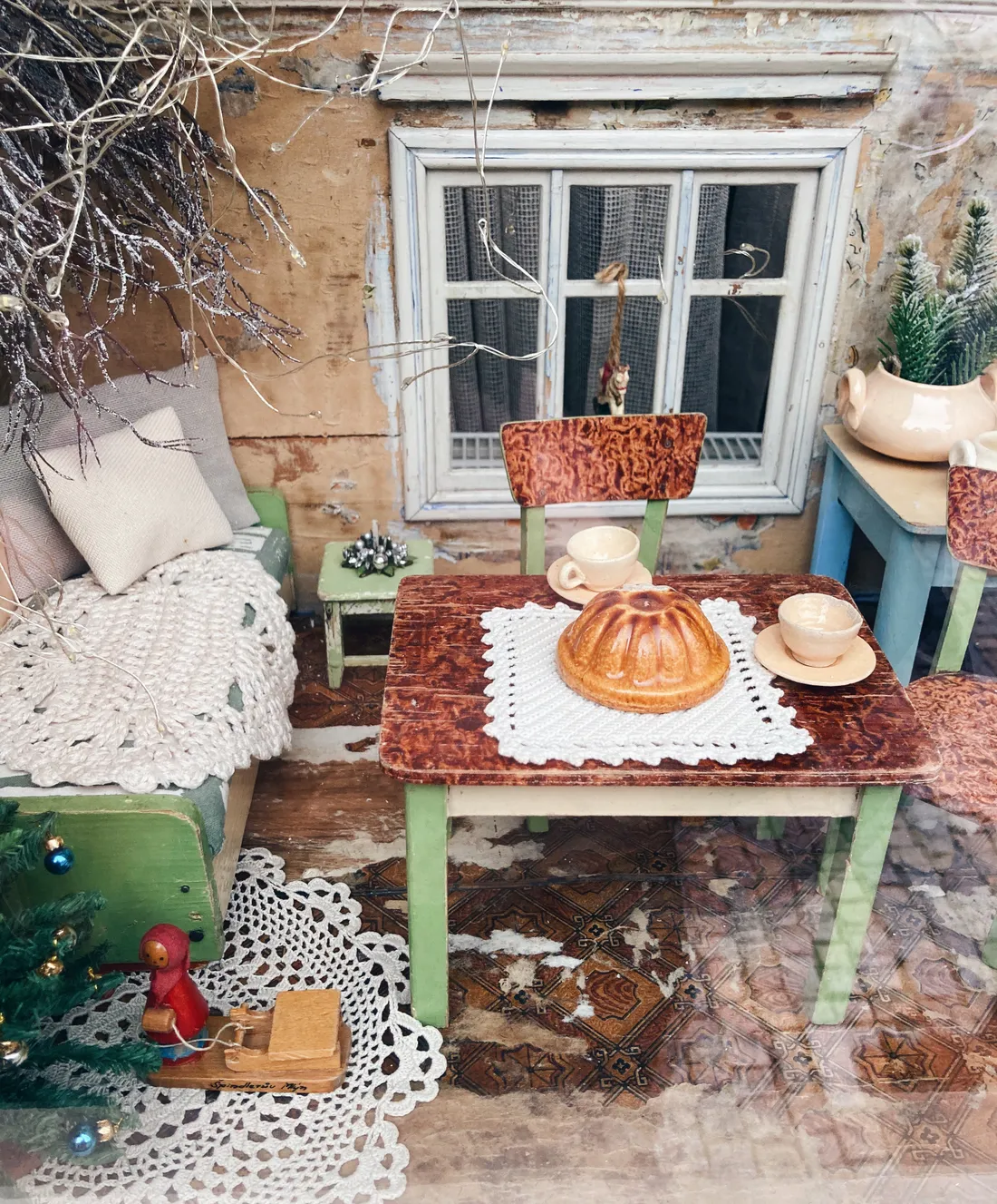 Miniatura rustikální místnosti s bábovkou, šálkem a vánočním stromkem v diorámu.