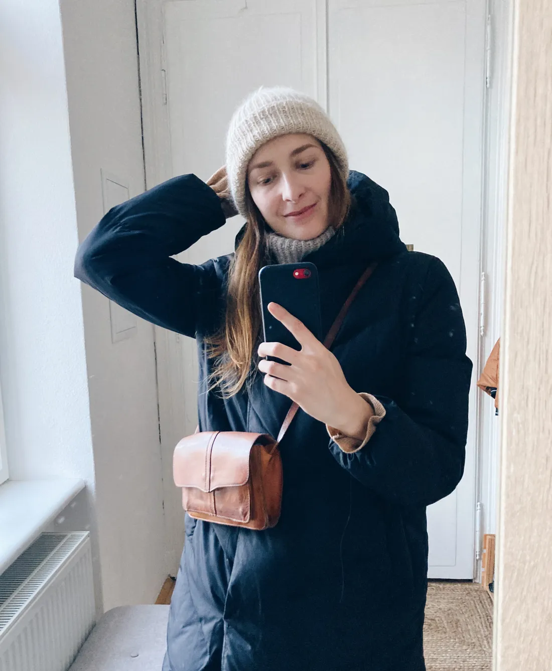 Zrcadlové selfie v černé zimní bundě, béžovém kulichu a hnědé kožené crossbody kabelce.